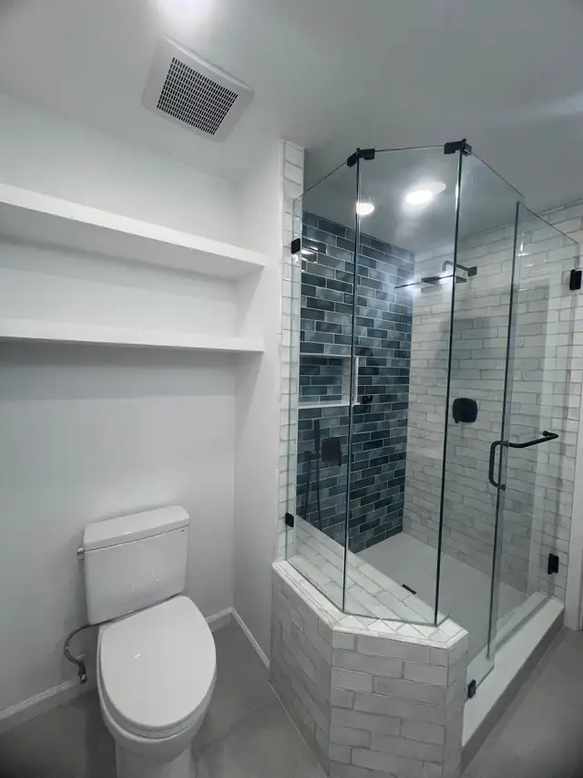 Corner walk-in shower with blue glass tile accent wall and frameless enclosure next to open storage shelves