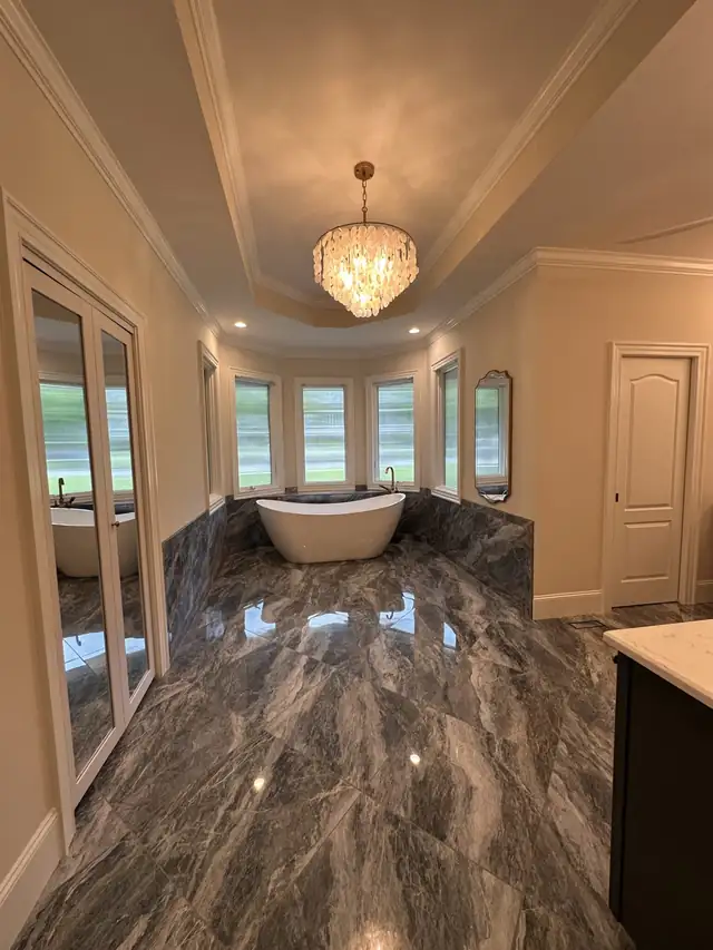 Frameless glass shower with bench and marble-look porcelain walls beside a wood double vanity with arabesque tile wall and black fixtures
