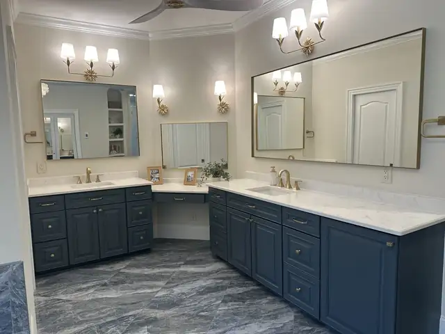Long primary bathroom with gray marble-look floor, crystal chandelier and freestanding tub under a bay window