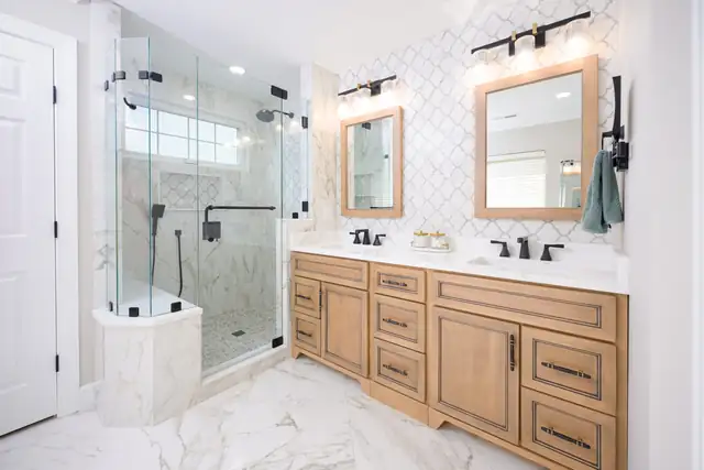 Primary bathroom remodel in the Triangle with navy double vanities, built-in makeup desk, brass sconces and gray marble-look floor tile