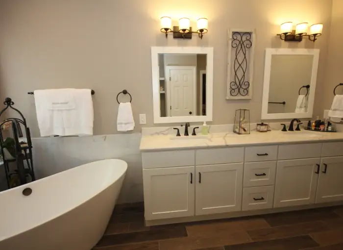 Remodeled bathroom with a freestanding soaking tub, a white double vanity, marble-look wainscot tile and bronze sconces