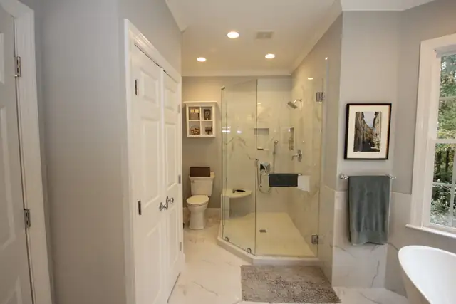 Remodeled bathroom with dark wood double vanity, framed mirrors, marble-look counter and frameless glass shower