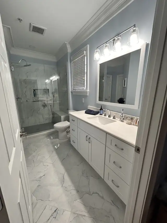 Bathroom with a white double vanity, a lighted mirror and a frameless glass shower with marble-look tile